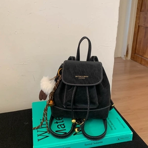 Close-up of black leather backpack featuring contrast stitching and white plush charm