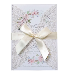 Macro view of laser-cut lace wedding invitation with cream silk ribbon and floral insert