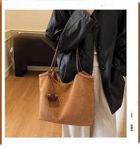 Detail of a brown suede tote bag with artistic letter embroidery and a small side pouch