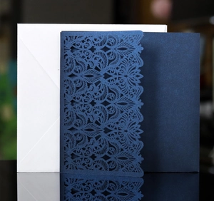 Detail of laser-cut navy blue wedding invitation with intricate floral patterns and envelope