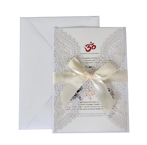 Detail of laser-cut lace wedding invitation with white satin ribbon and red Om symbol
