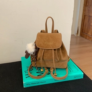 Close-up of brown leather mini backpack with gold logo, drawstring and fur ball charm