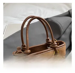 Detail of the knotted brown suede handle fixed with gold metal eyelets on a tote bag