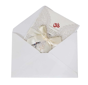 Detailed laser-cut white lace wedding invitation with a silk ribbon and Om symbol