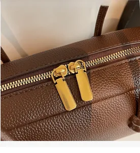 Close-up of smooth dual metal zippers and litchi texture on a brown bowling bag