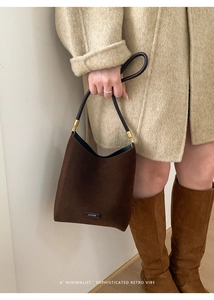 Detail of a brown suede tote bag featuring black leather handles and gold metal accents