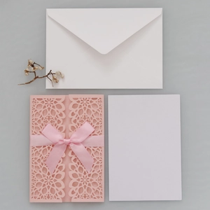 Detailed view of laser-cut pink wedding invitation with silk bow and matching envelope