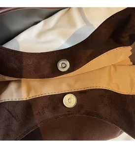 Detailed close-up of premium magnetic gold hardware on brown suede tote bag