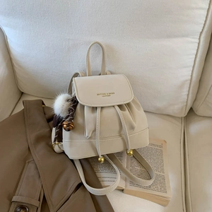 Detail of cream leather backpack featuring drawstring closure and golden ball pendant charm