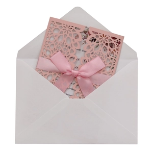 Detail of pink laser-cut wedding invitation with elegant silk ribbon bow and white envelope