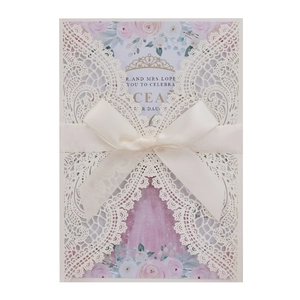 Detailed laser-cut ivory wedding invitation lace cover with pink floral insert and silk bow