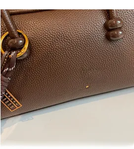 Detail of dark brown lychee leather handbag featuring gold hardware and a woven knot charm