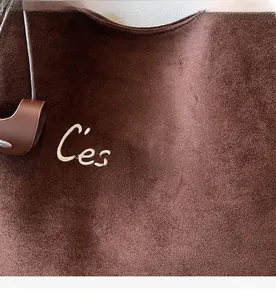 Detailed close-up of coffee brown suede tote bag with white letter embroidery