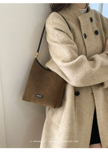 Close-up of brown suede bucket bag featuring slim black shoulder strap and logo tag
