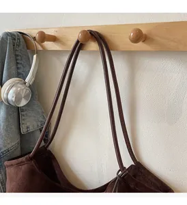Detail of dark brown suede tote bag with embroidery, slim leather handles on wooden hook