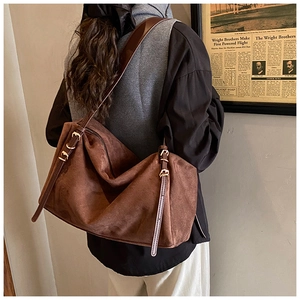 Close-up of brown suede shoulder bag showing adjustable leather strap and golden buckle detail