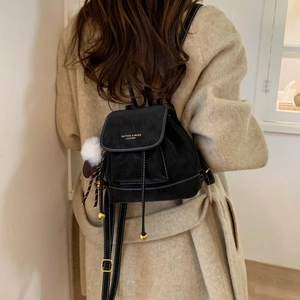 Detail of black matte leather backpack with white stitching and decorative pom-pom charm