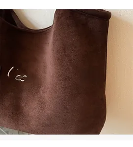 Close-up of brown suede tote bag featuring artistic white letter embroidery and soft texture