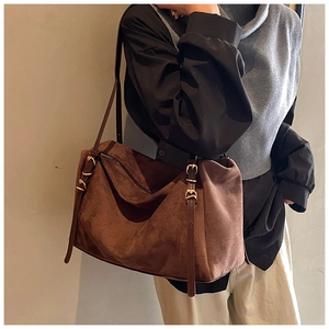 Detail of dark brown suede shoulder bag with matte texture and golden buckle on model