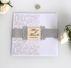 Close-up of laser-cut floral wedding invitation with silver glitter belt and custom name card