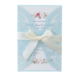 Detail of laser-cut lace wedding invitation with floral insert and beige satin ribbon