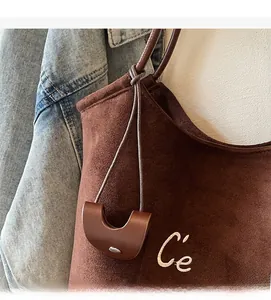 Macro shot of brown suede tote bag featuring white letter embroidery and round leather charm