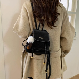 Detail of black mini backpack featuring white contrast stitching and plush ball charm