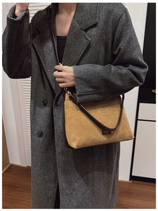 Primo piano di una borsa a secchiello in pelle marrone con dettagli in oro e cappotto