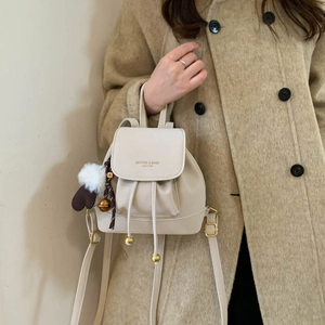 Detail of beige drawstring backpack with plush ball charm and gold buckle on a shoulder