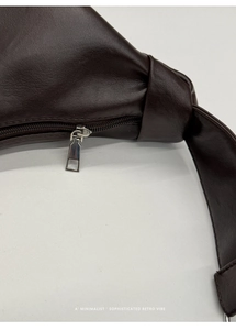 Close-up of retro dark brown leather dumpling bag with silver zipper and knot detail