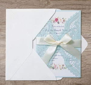 Detail of laser-cut lace wedding invitation with light blue sleeve and ivory satin bow