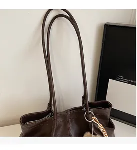 Détail d'un sac cabas marron foncé avec poignées fines et bijou de sac à pompon