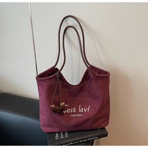 Detail of burgundy suede tote bag featuring white letter embroidery and leather straps
