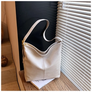 Détail du sac seau en similicuir crème avec boucles dorées sur une table en bois