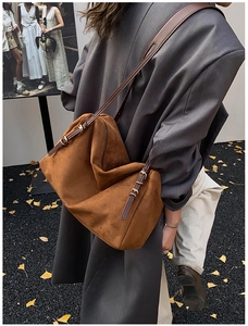 Detail of brown suede tote bag with golden buckles on shoulder strap worn by model