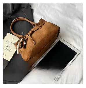 Brown suede tote bag with tricolor bead charm and decorative buckle on a stylish setting