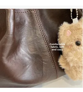 Détail de la texture cuir marron foncé avec coutures et breloque pendentif ours peluche