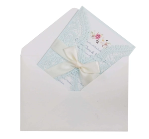 Detailed laser cut lace wedding invitation with a light blue shell and white silk ribbon