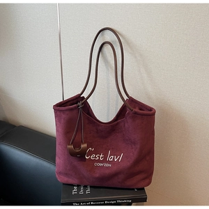 Detail of burgundy suede tote bag featuring white letter embroidery and brown handles