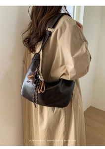 Detail of dark brown hobo bag with knotted strap and tassel charm on a trench coat