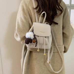 Detailed view of the drawstring closure on a cream mini backpack with plush charms