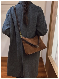 Dettaglio di borsa a secchiello in camoscio marrone con hardware dorato su cappotto grigio