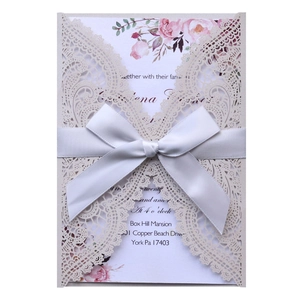 Detail of laser-cut lace wedding invitation with white satin bow and floral inner card