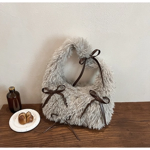 Dettaglio della borsa in peluche grigia con fiocchi marroni e stemma in metallo argento