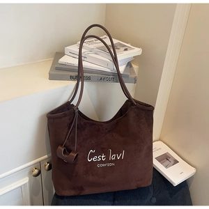 Detail of dark brown faux suede tote bag with white embroidery next to aesthetic books