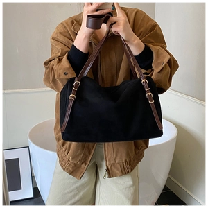 Detail of minimalist black tote bag with brown leather straps and gold metal buckles
