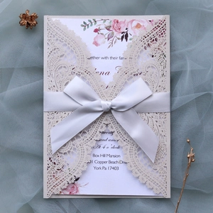 Close-up of laser-cut white lace wedding invitation with ribbon and floral pattern