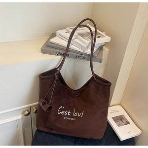 Detail of coffee suede tote bag featuring white letter embroidery and leather strap