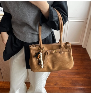 Detail of caramel brown matte leather tote with beaded charm and metal buckle design