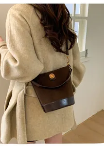 Detail of a dark brown suede bucket bag with gold hardware worn by a model in a beige coat